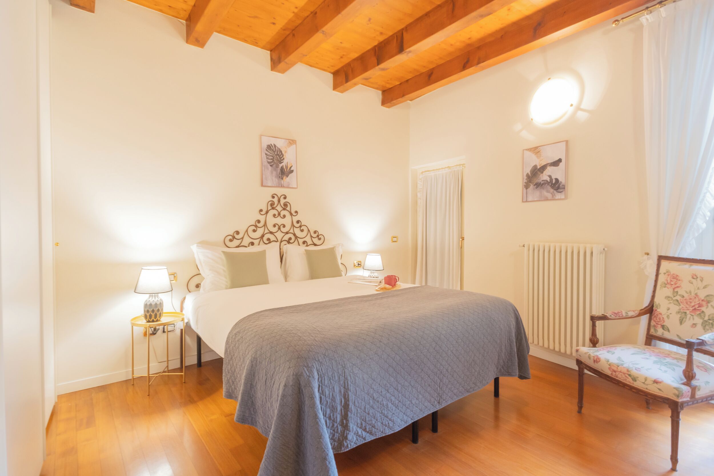 Un dormitorio con una cama grande, piso de madera, un radiador, una silla y dos lámparas fijadas a la pared.