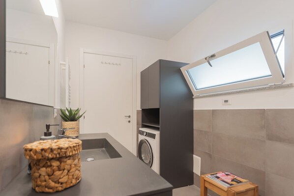 Un baño moderno con lavamanos, lavadora, espejo y ventana.