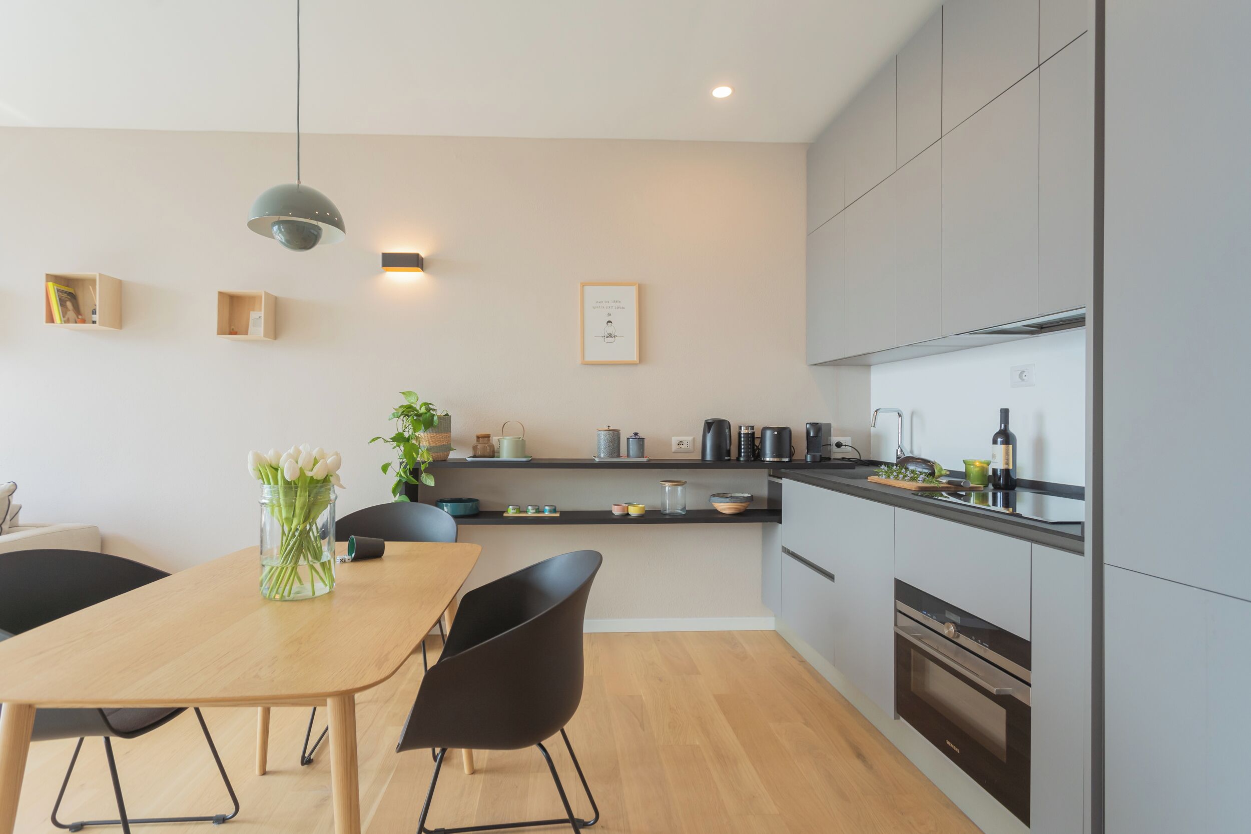 A modern kitchen with a dining area, wooden table, black chairs, and a pendant light.