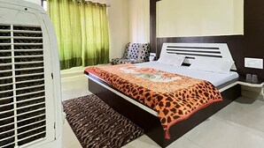 Une chambre à coucher comprenant un lit, une table de chevet, un téléviseur fixé au mur et un ventilateur de plafond.