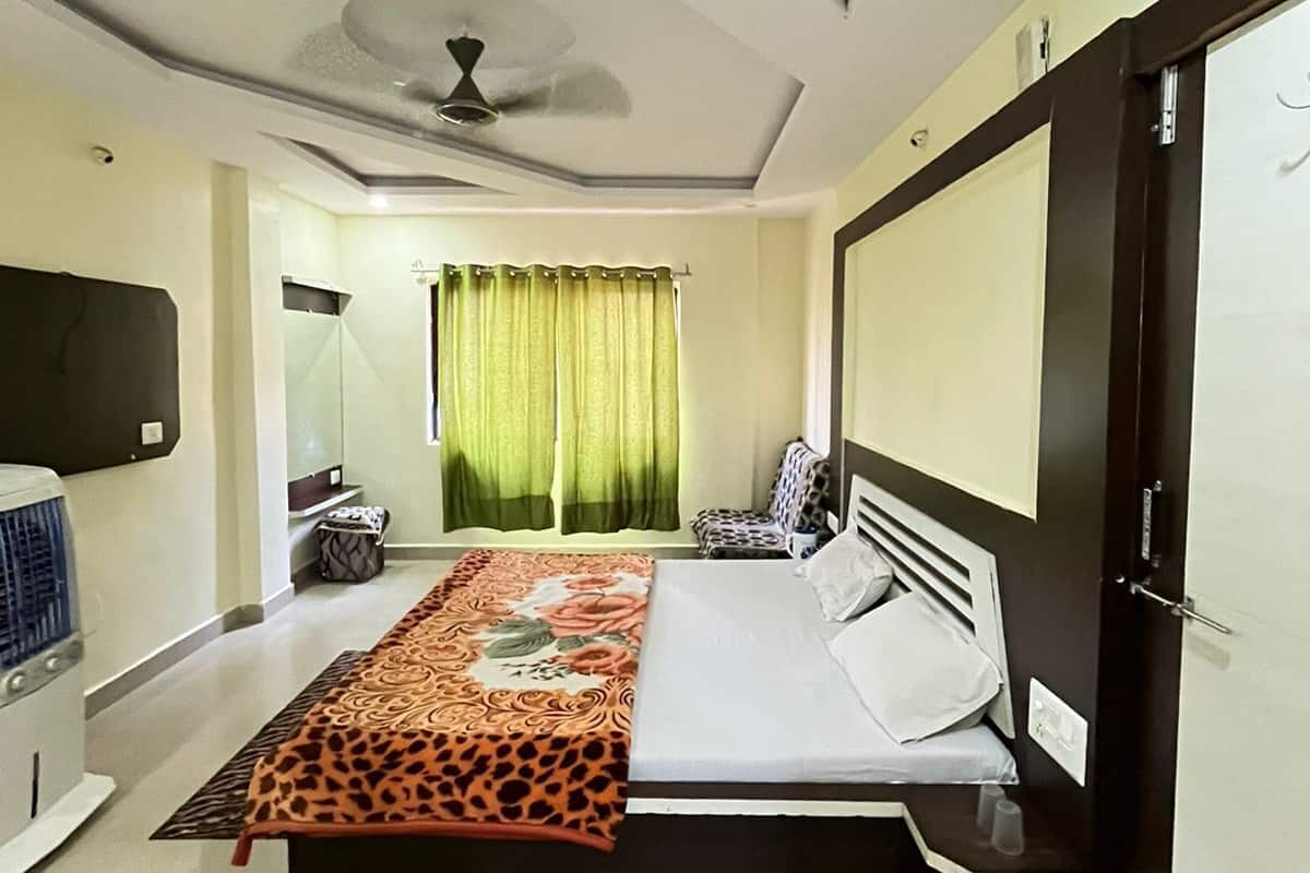 Une chambre à coucher avec un lit, un ventilateur de plafond, une télévision et une fenêtre avec des rideaux.