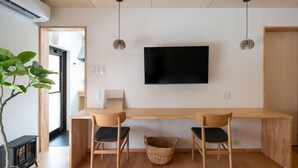 Una sala de estar moderna con un televisor montado en la pared, dos sillas de madera, una mesita y una planta en maceta.