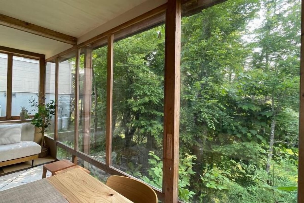 A room with a large window, a wooden table, a sofa, and a potted plant.