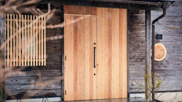 Una puerta de madera con un picaporte negro, una tabla de madera vertical y un letrero redondo de madera en la pared.