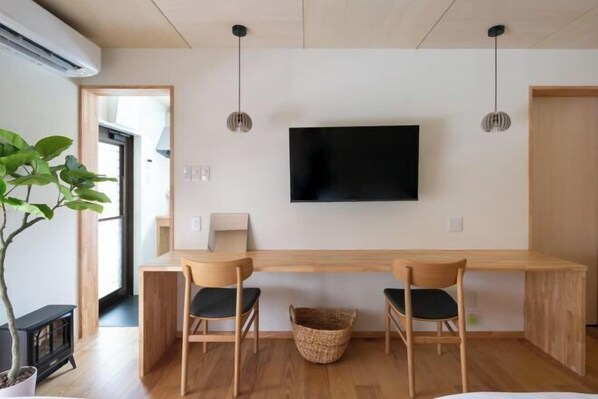 A modern living room with a wooden dining table, two chairs, a TV mounted on the wall, and a potted plant. - Cooee Yamanakako (Yamanakako)
