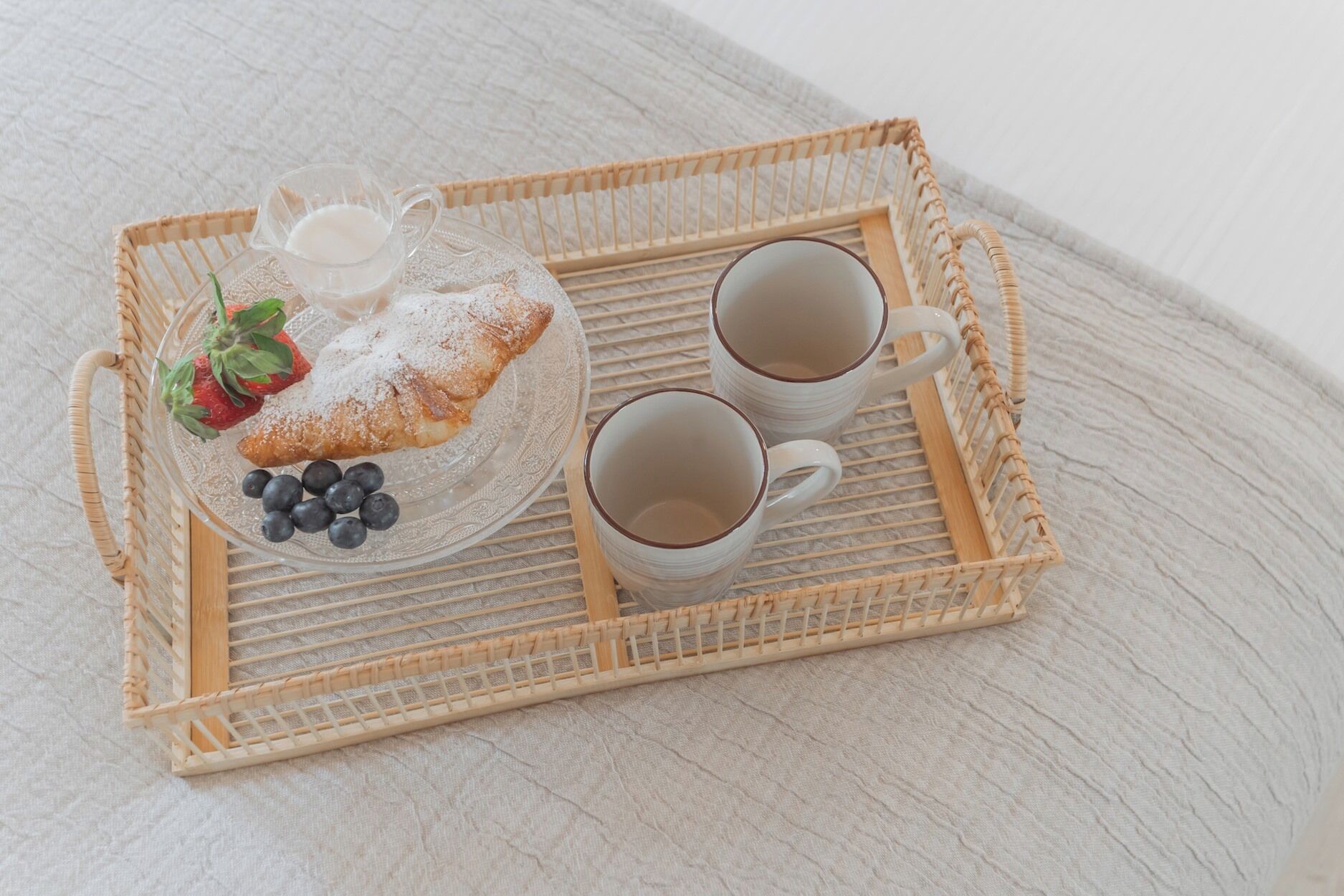 Una bandeja con un pastel, fresas, arándanos y dos tazas de café sobre una superficie texturizada.