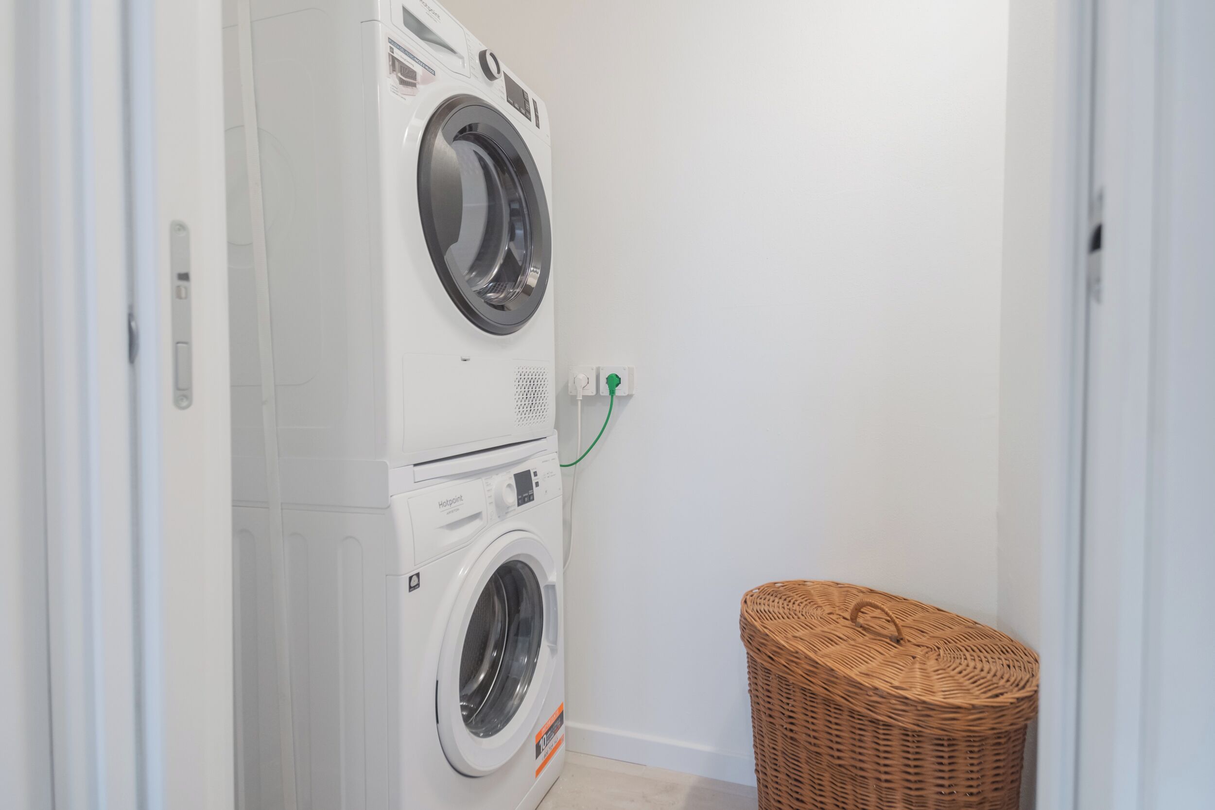A laundry room with two stacked front-loading washing machines and a wicker basket.