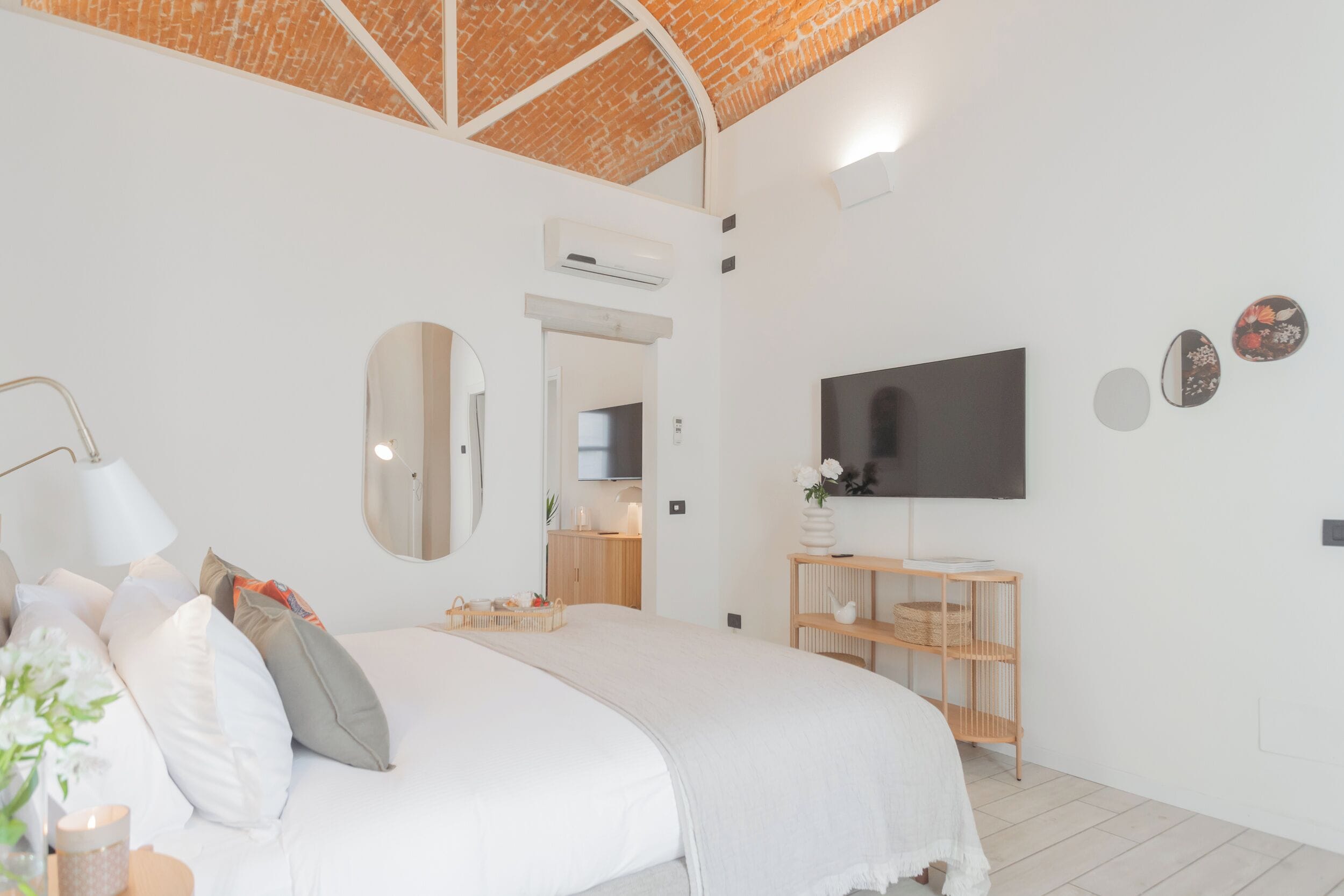 Un dormitorio moderno con una cama grande, un televisor montado en la pared, una mesita de noche de madera y un techo de ladrillo.