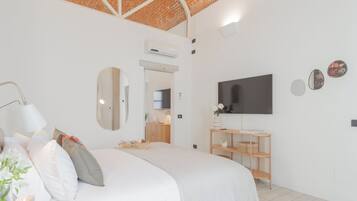 Un dormitorio moderno con una cama grande, un televisor montado en la pared, una mesita de noche de madera y un techo de ladrillo.