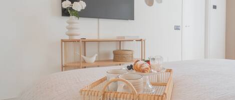 A neatly arranged bedroom with a bed, bedside tables, a TV, and a tray with breakfast items.