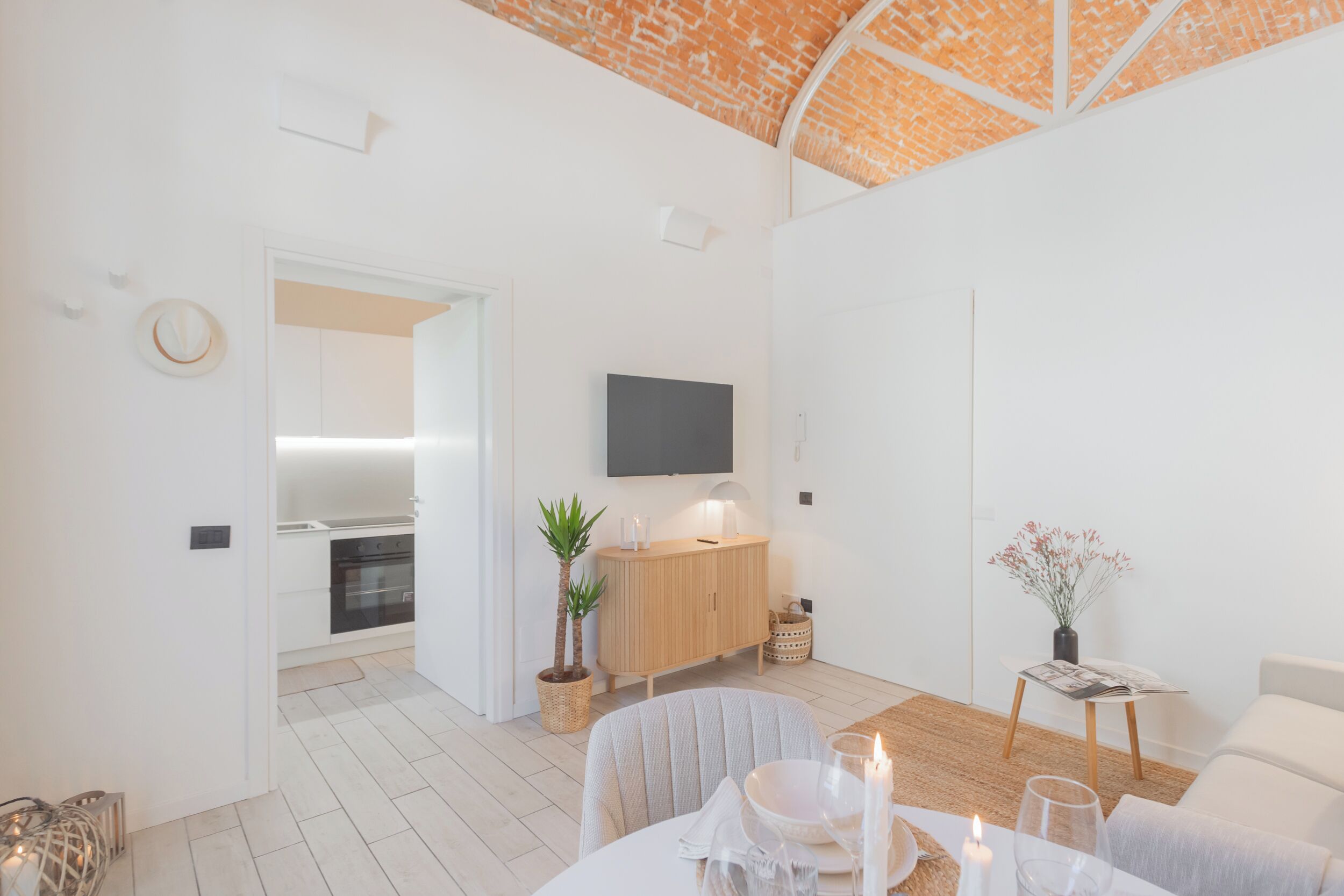 Un soggiorno moderno con una cucina sullo sfondo, una televisione a schermo piatto montata a parete e un'area pranzo con un tavolo apparecchiato per due persone.