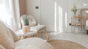 Ein modernes Wohnzimmer mit einer Couch, einem runden Couchtisch, einem Sessel und einem kleinen Beistelltisch mit Lampe und Blumen.'