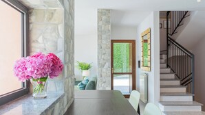 A modern interior with a stone wall, a dining area with a table and chairs, and a staircase with a black railing.