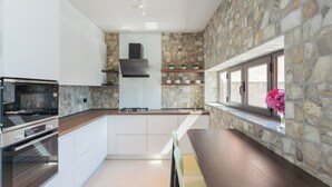A modern kitchen with stone walls, built-in appliances, and a window with a flower vase.