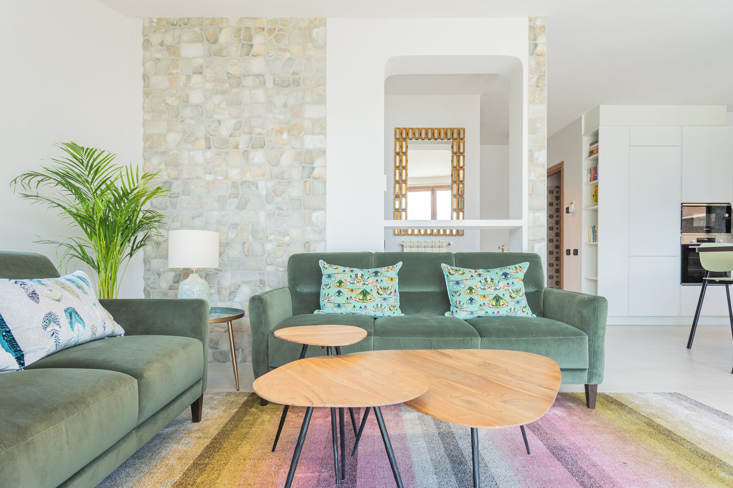 Una sala de estar moderna con un sofá verde, dos mesitas de madera y una alfombra colorida.