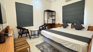 A modern hotel room with a large bed, a small desk, a chair, a round table, and a wardrobe. - Hotel Insta 18 (Siliguri)