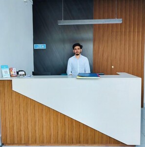 A reception desk with a modern design, featuring a wooden panel and a white counter. A sign on the wall indicates a recycling bin. - Hotel Insta 18 (Siliguri)