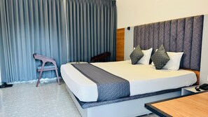 Una habitación de hotel con una cama grande, un cabecero de madera, cortinas grises, una mesita de noche de madera y un teléfono.