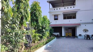 A two-story building with a paved courtyard, surrounded by lush greenery and a small waterfall feature. - Hotel Insta 18 (Siliguri)
