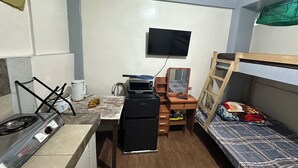 Ein gemütlicher Raum mit Küchenzeile, einem kleinen Tisch, einem Bett mit Holzleiter, einem Fernseher und einem Spiegel.