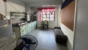 Eine kleine Küche mit Kühlschrank, Spüle und einem Fenster mit rosa Vorhängen. Es gibt eine kleine Sitzecke mit einem Sessel und einer Couch.