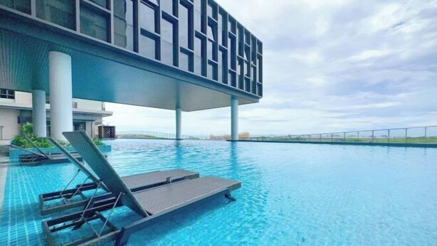 A modern hotel with a large infinity pool, lounge chairs, and a clear view of the horizon.