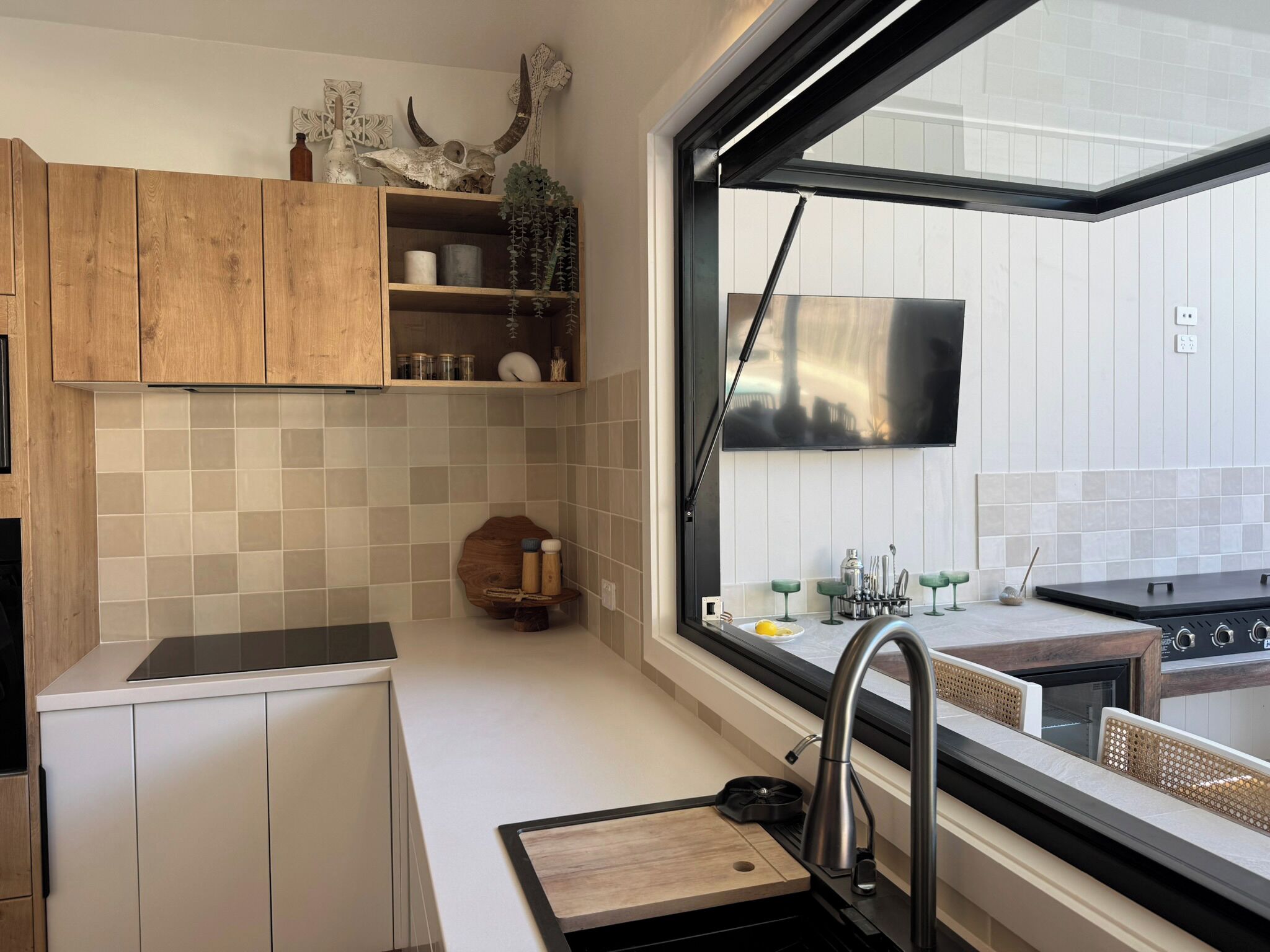 Cozinha moderna com armários de madeira, fogão embutido, uma janela ampla e vista para o exterior.