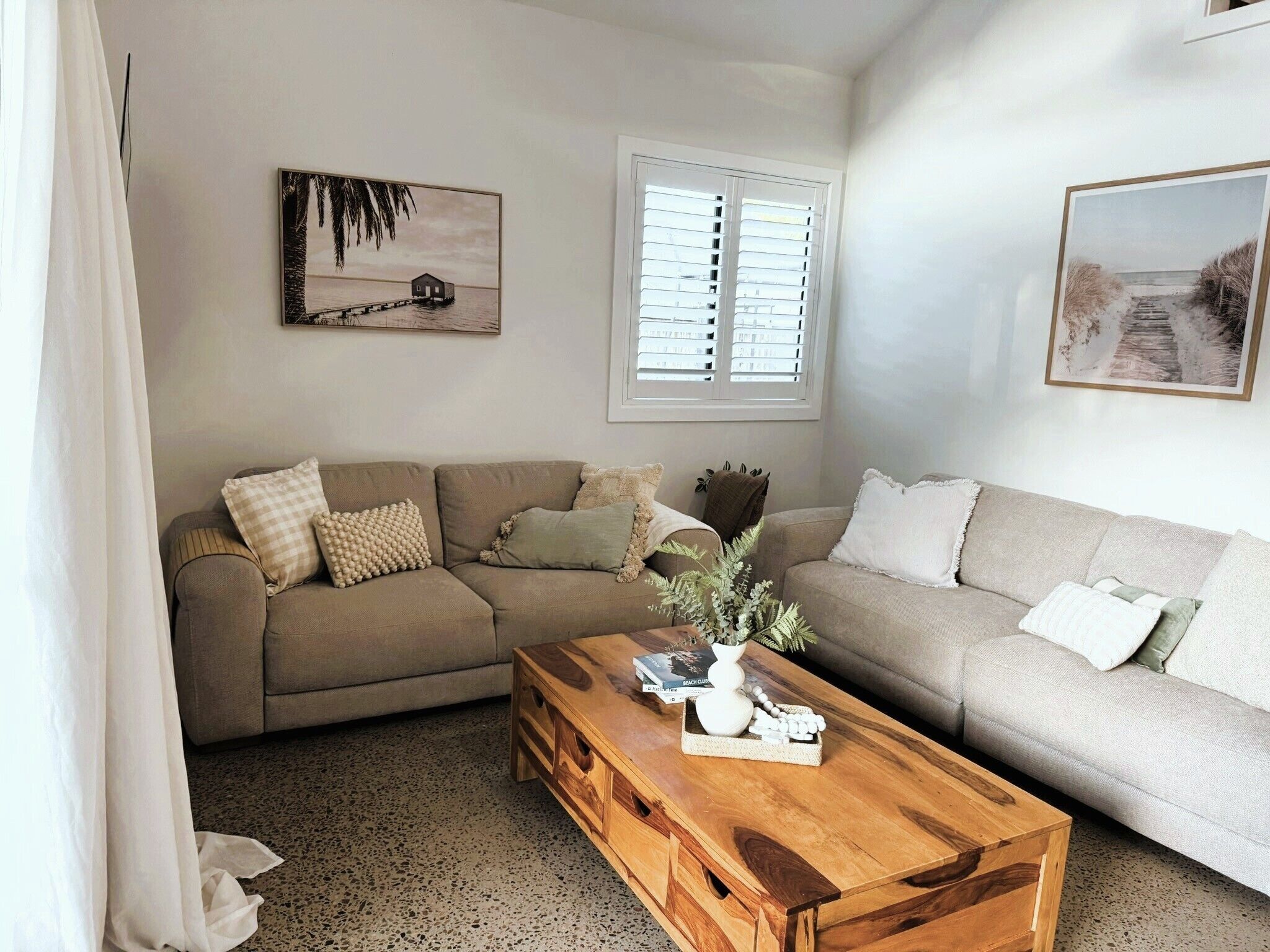 A living room with a beige sofa, a wooden coffee table, and two framed pictures on the wall.
