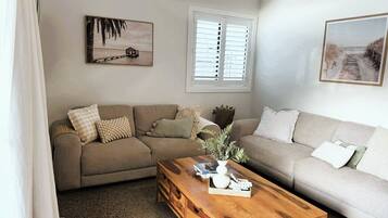 A living room with a beige sofa, a wooden coffee table, and two framed pictures on the wall.
