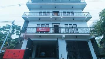 A multi-story building with a red sign, balconies, and a gated entrance.