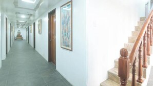 A hotel hallway with a tiled floor, wooden doors, and a staircase with wooden balusters.