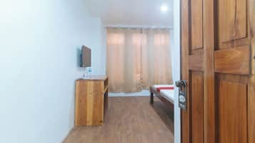 Una habitación pequeña con un escritorio de madera, una cama, un televisor montado en la pared y una puerta con cerradura.