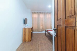 A small room with a wooden desk, a bed, a television mounted on the wall, and a door with a lock. - RedDoorz @ Minas Place 2 Banez Ville Tacloban (Tacloban)