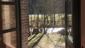 Ein Zimmer mit großem Fenster und Blick auf eine grüne Fläche mit Bäumen und einer Ziegelmauer.