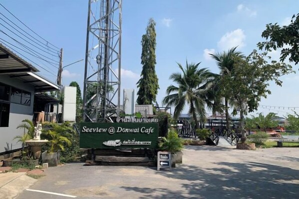 A sign for Seeview @ Donwil Cafe with a clear view of the surrounding area including a tall structure, palm trees, and a building with a sloped roof.