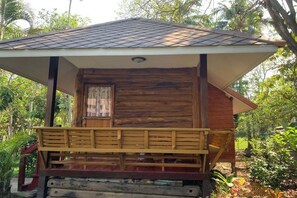 A wooden cabin with a porch, a window with curtains, and a sloped roof.