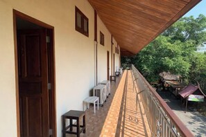 A covered balcony with a wooden ceiling, air conditioning units, and a view of the surrounding greenery.