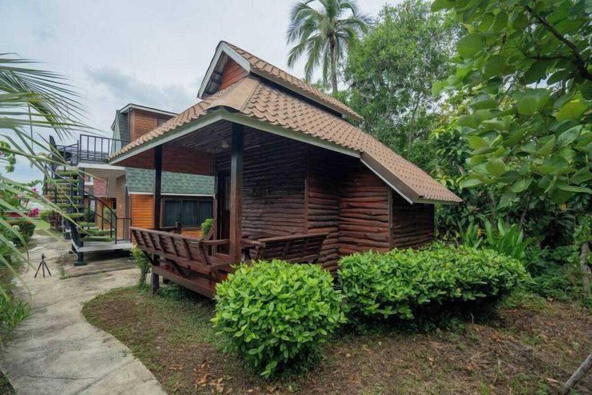 Uma cabana de madeira com varanda, rodeada por vegetação exuberante.