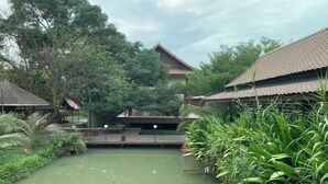 A traditional building with a tiled roof, surrounded by lush greenery and a small water channel. - Ban Suan Bang Toei Villa (Sam Phran)