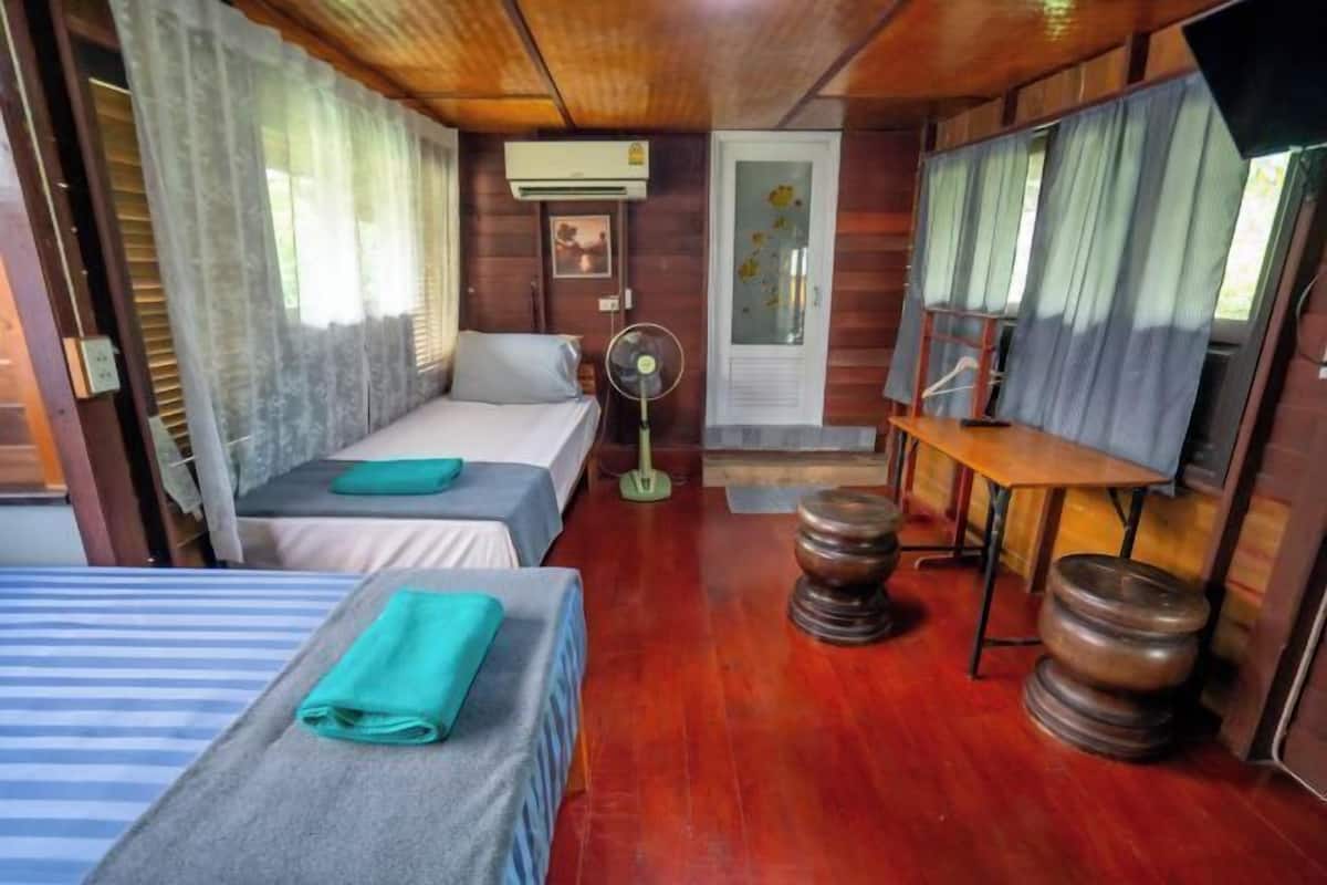 Uma cabana com duas camas, um ventilador, uma TV e móveis de madeira.