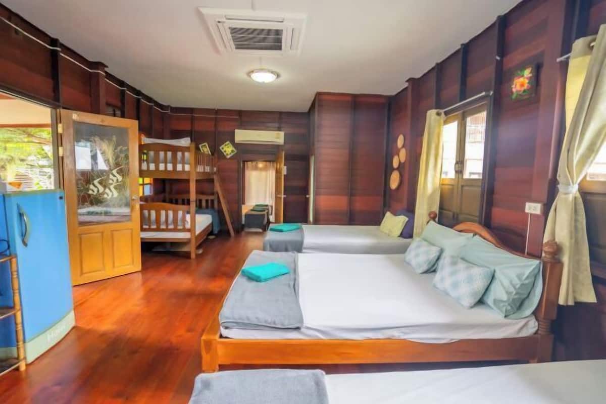 Quarto com duas camas, piso de madeira, guarda-roupa e janela com cortinas.