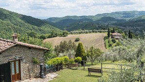 A stone house with a wooden door, a bench, and a view of rolling hills and fields. - The Barn apartment in farmhouse with swimming pool surrounded by greenery (Toscana)