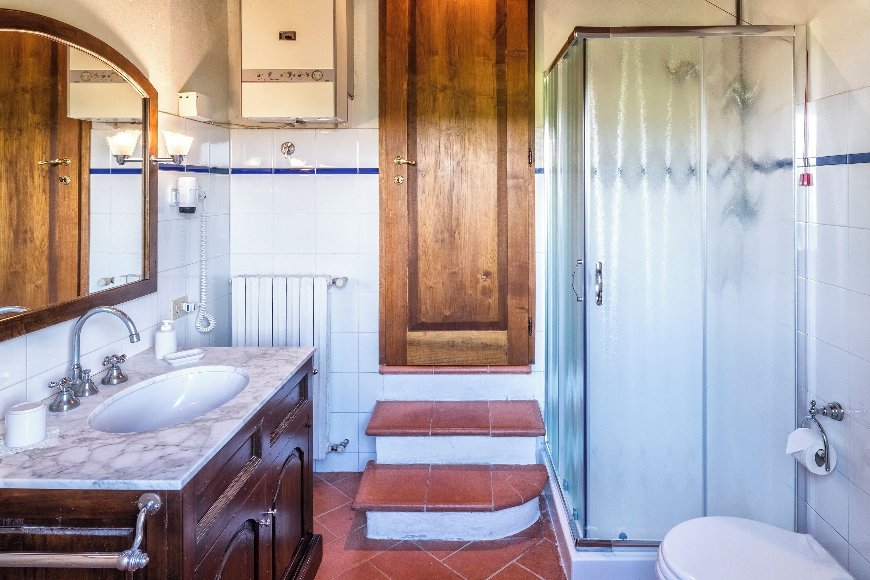 Une salle de bain avec un lavabo en marbre, des meubles en bois, une cabine de douche en verre et des toilettes blanches.