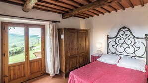 A bedroom with a wooden wardrobe, a bed with a metal headboard, and a view of the outdoors through a door. - The Barn apartment in farmhouse with swimming pool surrounded by greenery (Toscana)