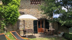 A stone building with a patio area featuring two lounge chairs, a table, and an umbrella. - The Barn apartment in farmhouse with swimming pool surrounded by greenery (Toscana)