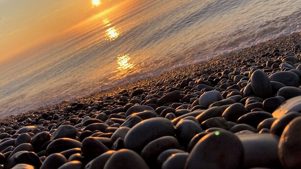Ein felsiger Strand mit Sonnenuntergang über dem Wasser.