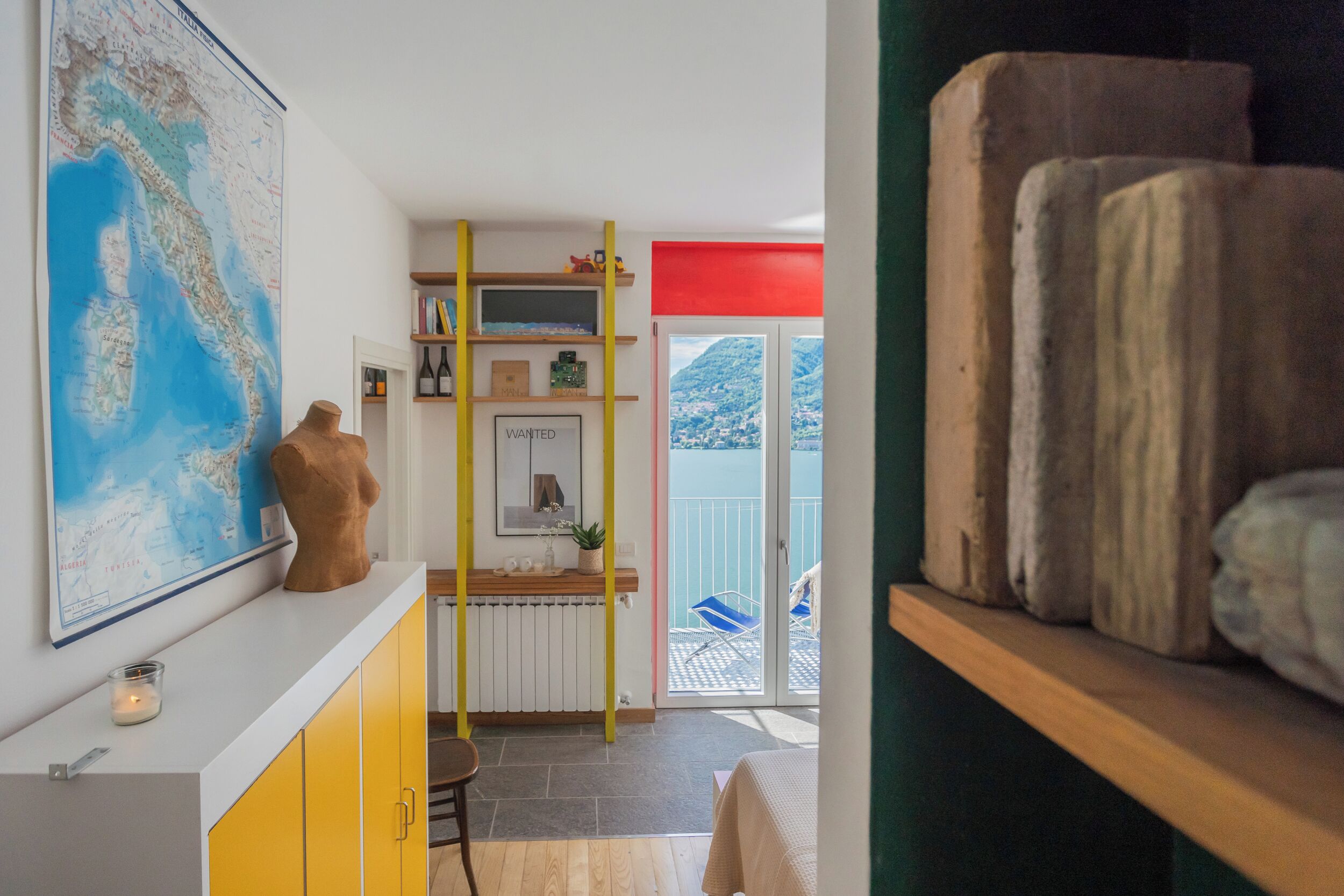 Una habitación con un mapa, una escultura de madera, una escalera, una pared roja y un balcón con una silla.