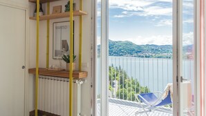 Habitación con vistas a un lago y montañas, un balcón con una silla, y estantes con libros y objetos decorativos.