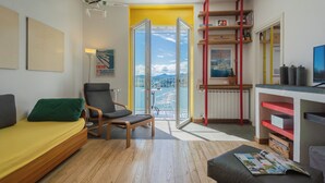 Una sala de estar moderna con un sofá, una silla, una mesita y un balcón con vistas a la ciudad.