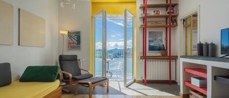A modern living room with a sofa, a chair, a small table, and a balcony with a view of the city.